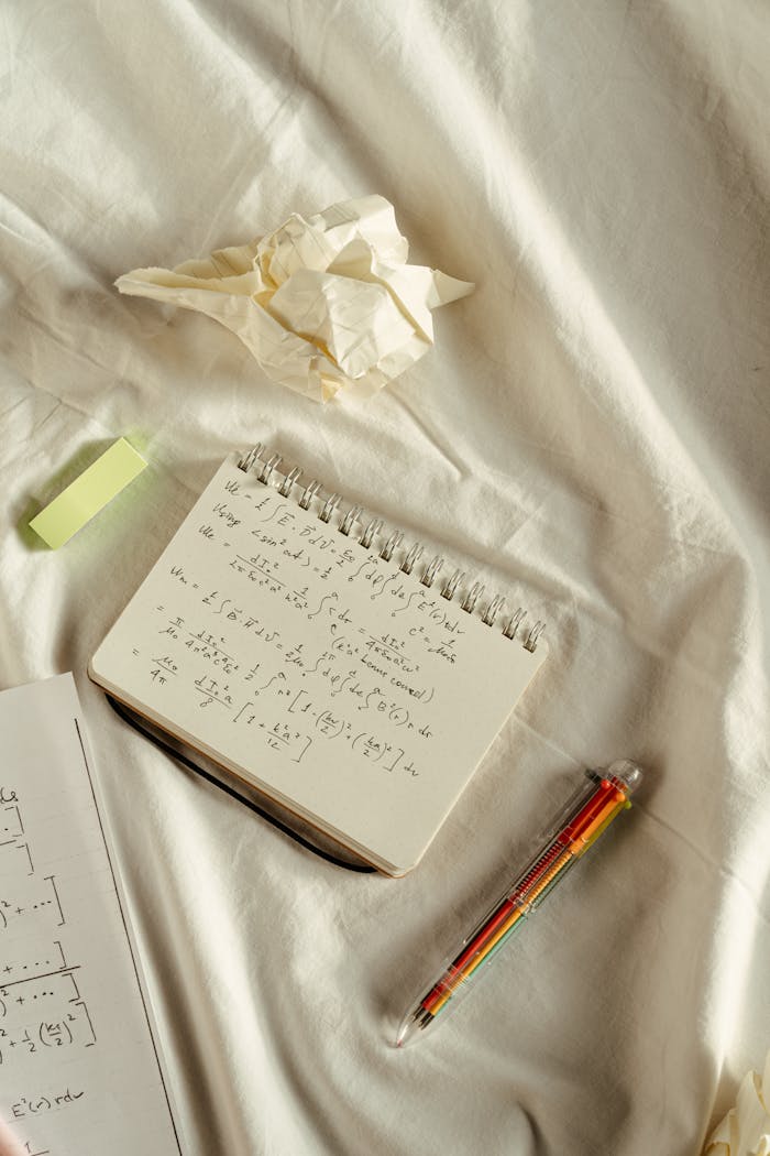 services-04 Handwritten math equations on a notebook placed on a crumpled bed sheet. Educational setup.