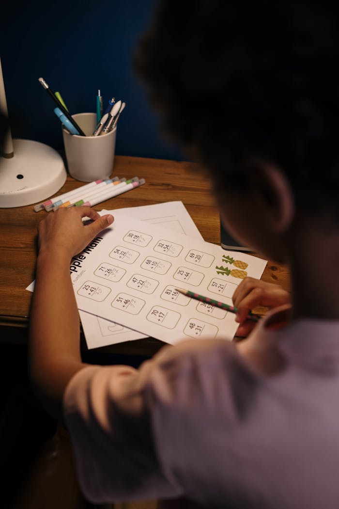 A student studying math problems at a desk, illuminated by a lamp. Educational setting.